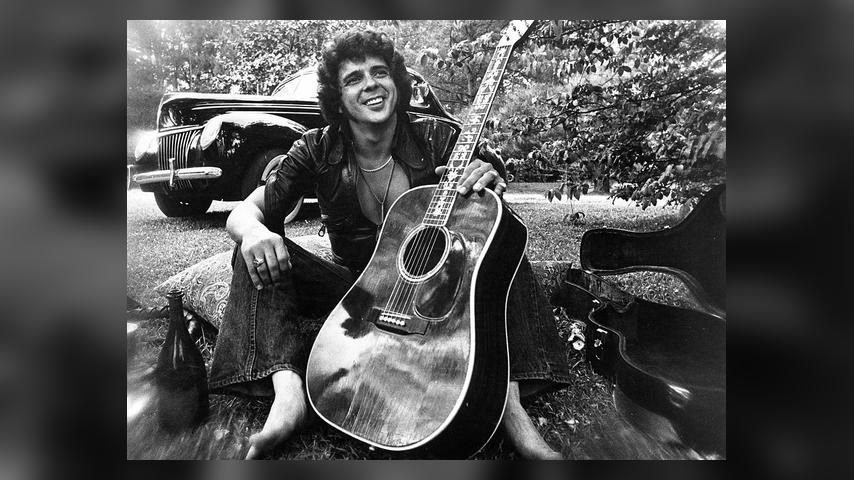 1975: Songwriter and guitarist Bobby Whitlock poses for a portrait in front of an old car next to a bottle of Dom Perignon champagne holding an acoustic guitar in circa 1975. (Photo by Michael Ochs Archives/Getty Images)
